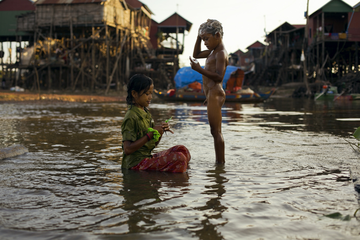 Deti v Kambodži sa umývajú v jazere Tonle Sap, okolo domy na koloch. Kambodža na motorke Honda Win. 
